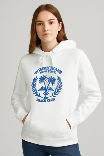 Woman wearing white embroidered Beach Club hoodie with blue palm tree crest